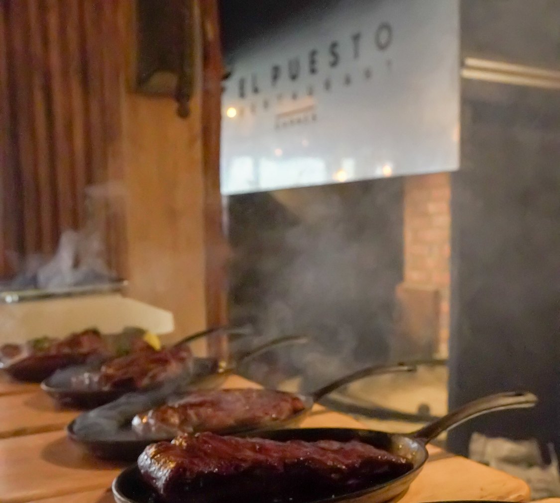 Interior de El Puesto Restaurant con platos de carne recien saliendo de la parrilla en Puerto Varas